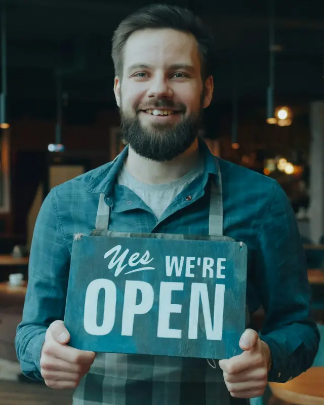 A café owner holding an Open sign